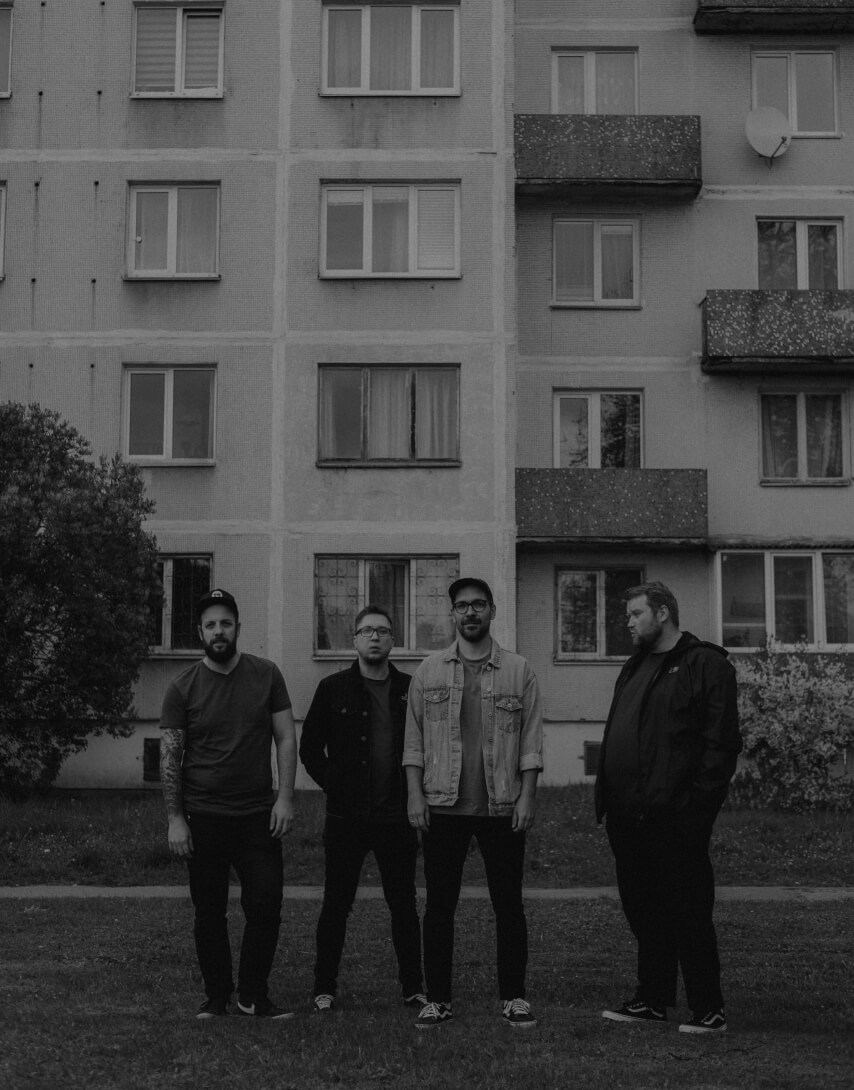 Black and white image of the four Have No Heroes punk rock band members standing in front a soviet 9 storey building